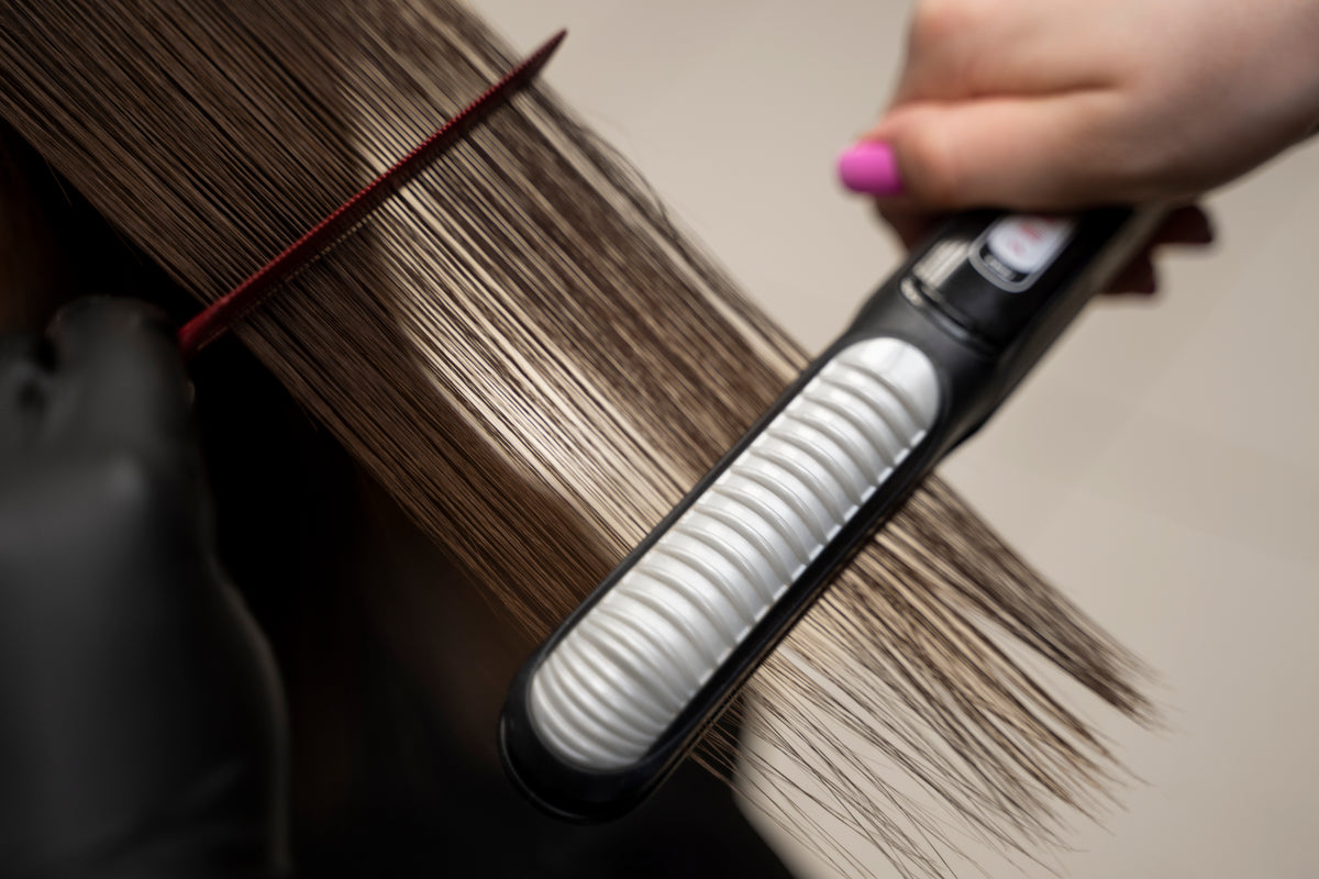 Estilista alisando el cabello con plancha profesional — tratamiento de alisado capilar